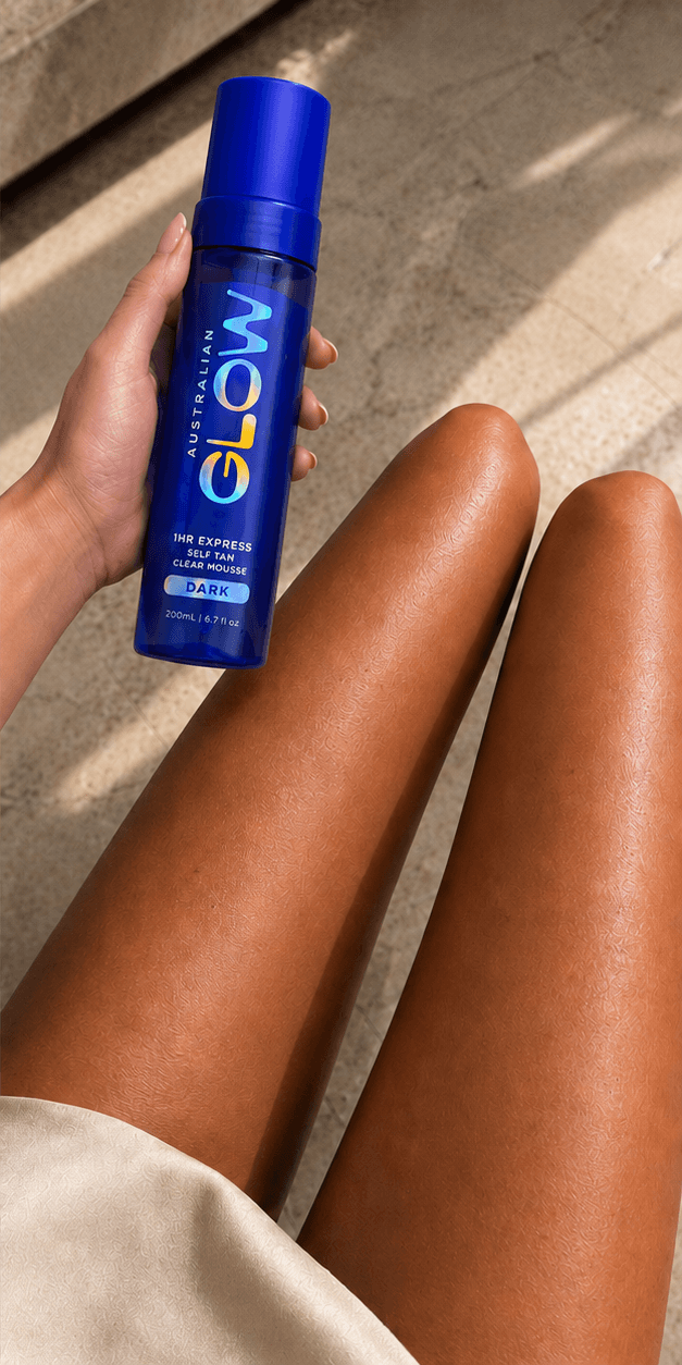 Self-tan after — light-olive legs after the 1Hr Clear Mousse Dark — deep cocoa bronze, hand holding the cobalt bottle
