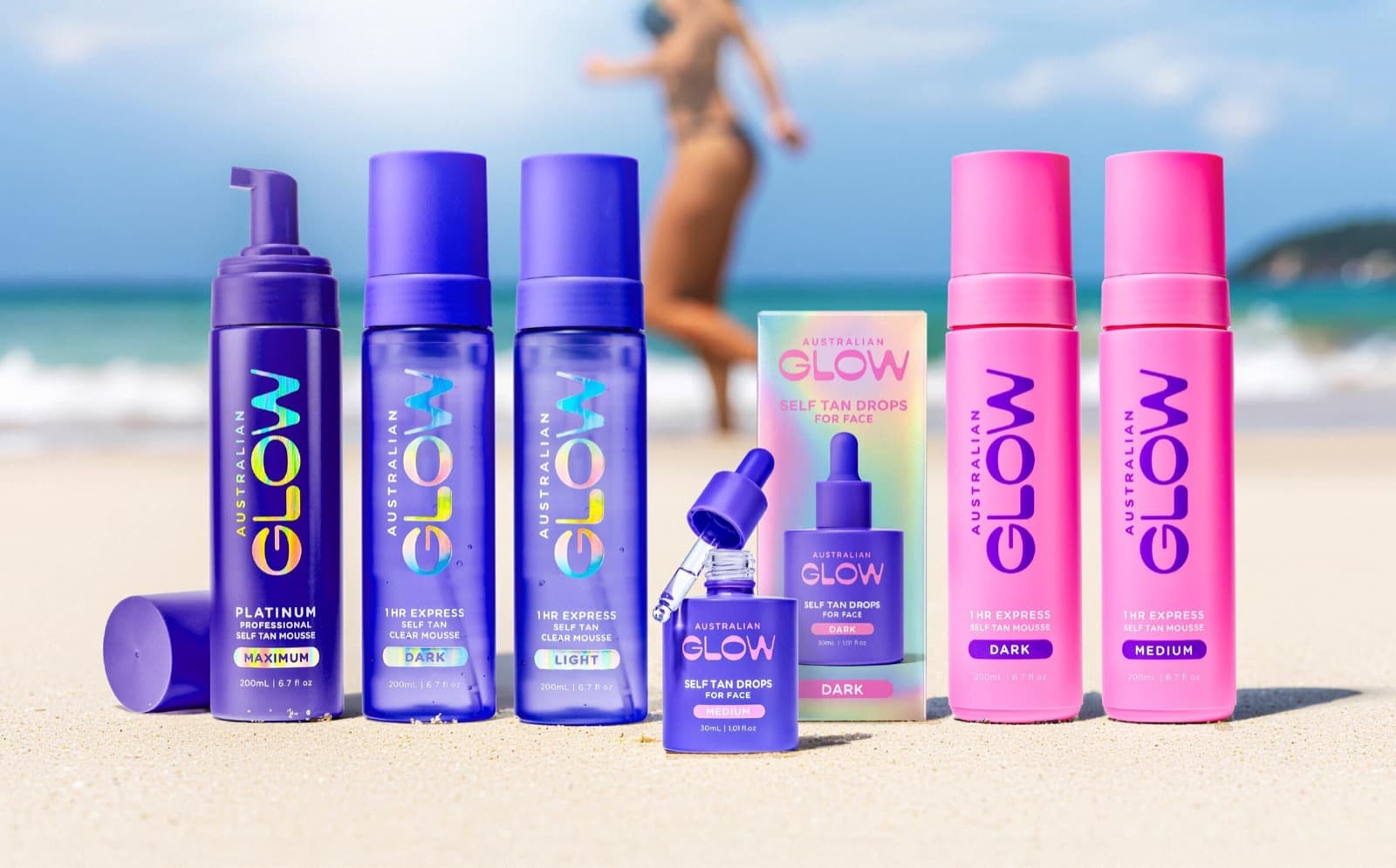The full Australian Glow range lined up in the sand — Platinum, Clear Mousse, Face Tan Drops and Express Mousse