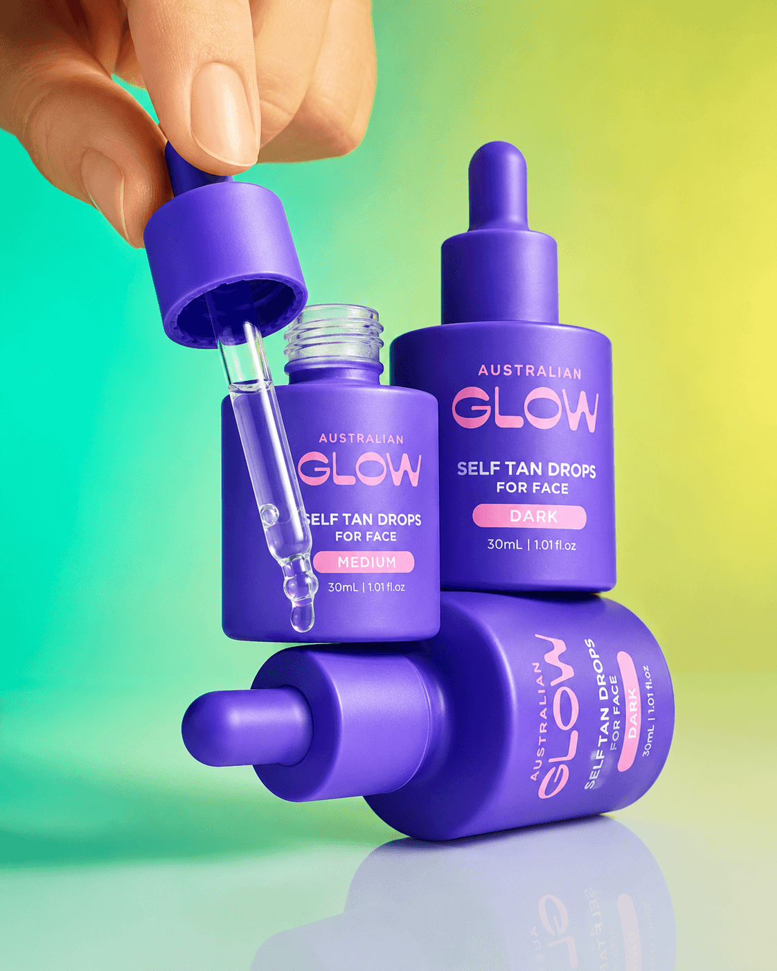 Australian Glow Face Tan Drops — hand mid-extraction with three product bottles